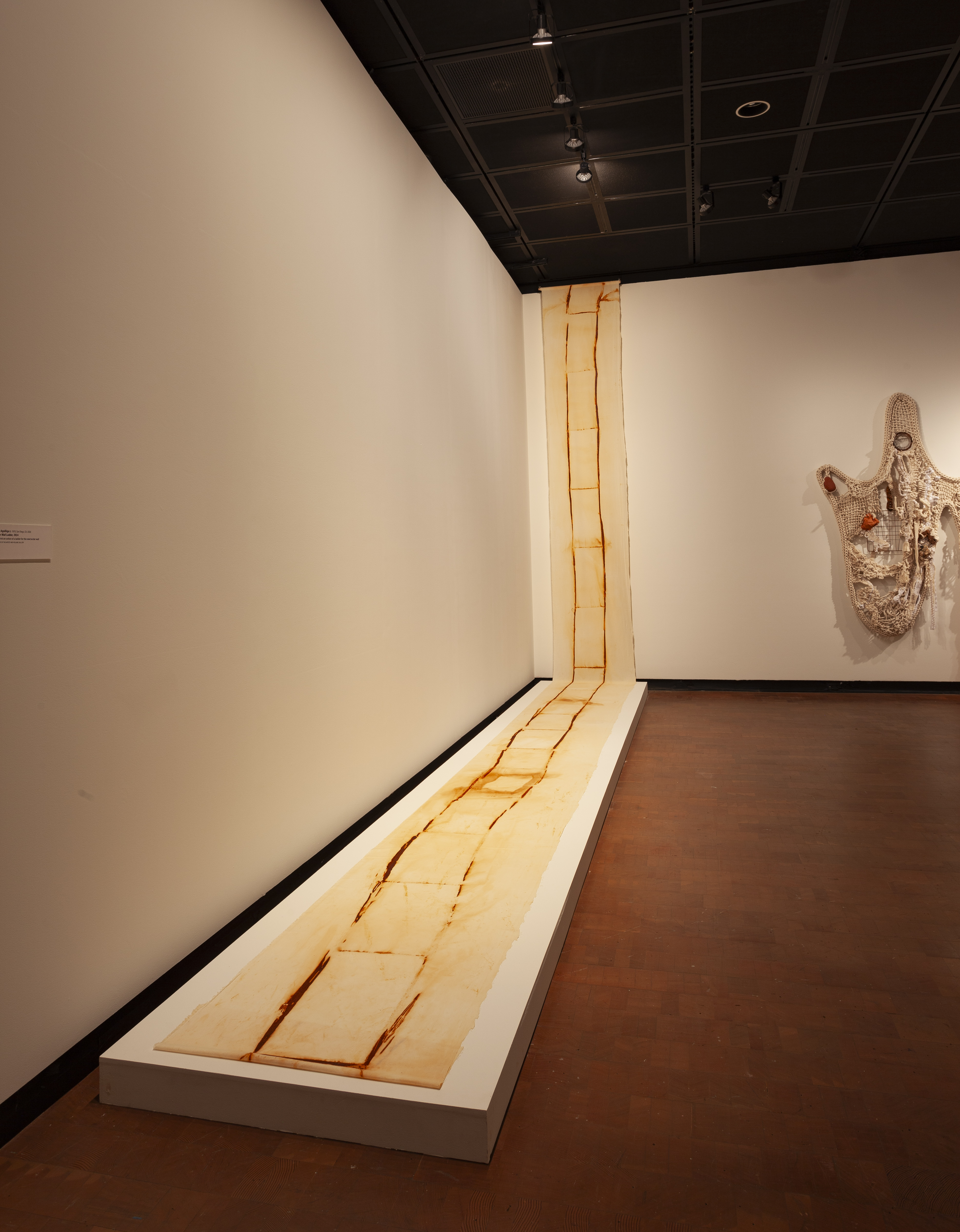 An artists rendering of a ladder on fabric extends along the floor and wall of a gallery.