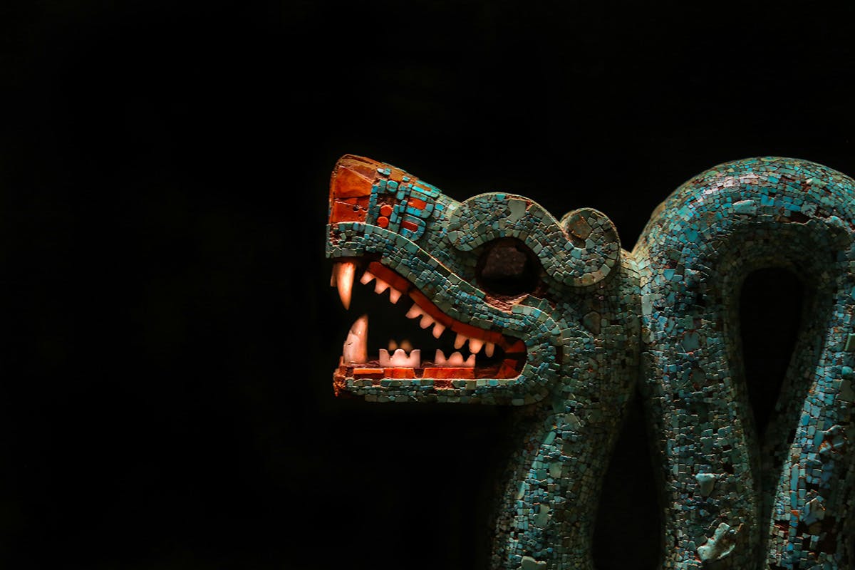 A stone dragon artifact pictured against a black backdrop.  the dragon is green with red teeth and nose