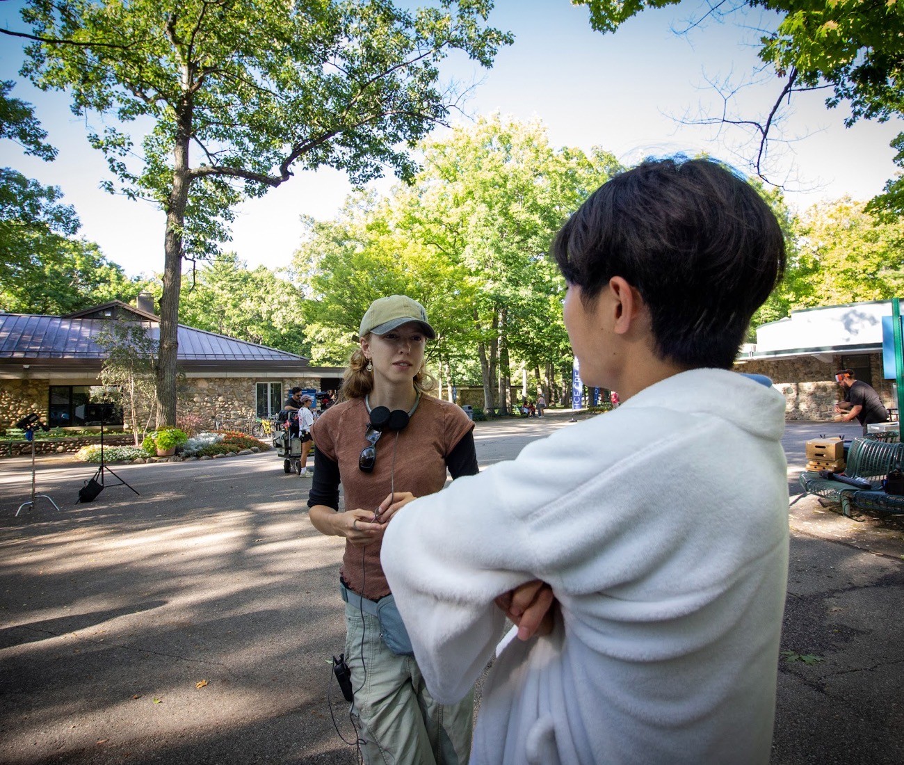 A young female film director speaks to an actor on the set of a film near a lakeside.