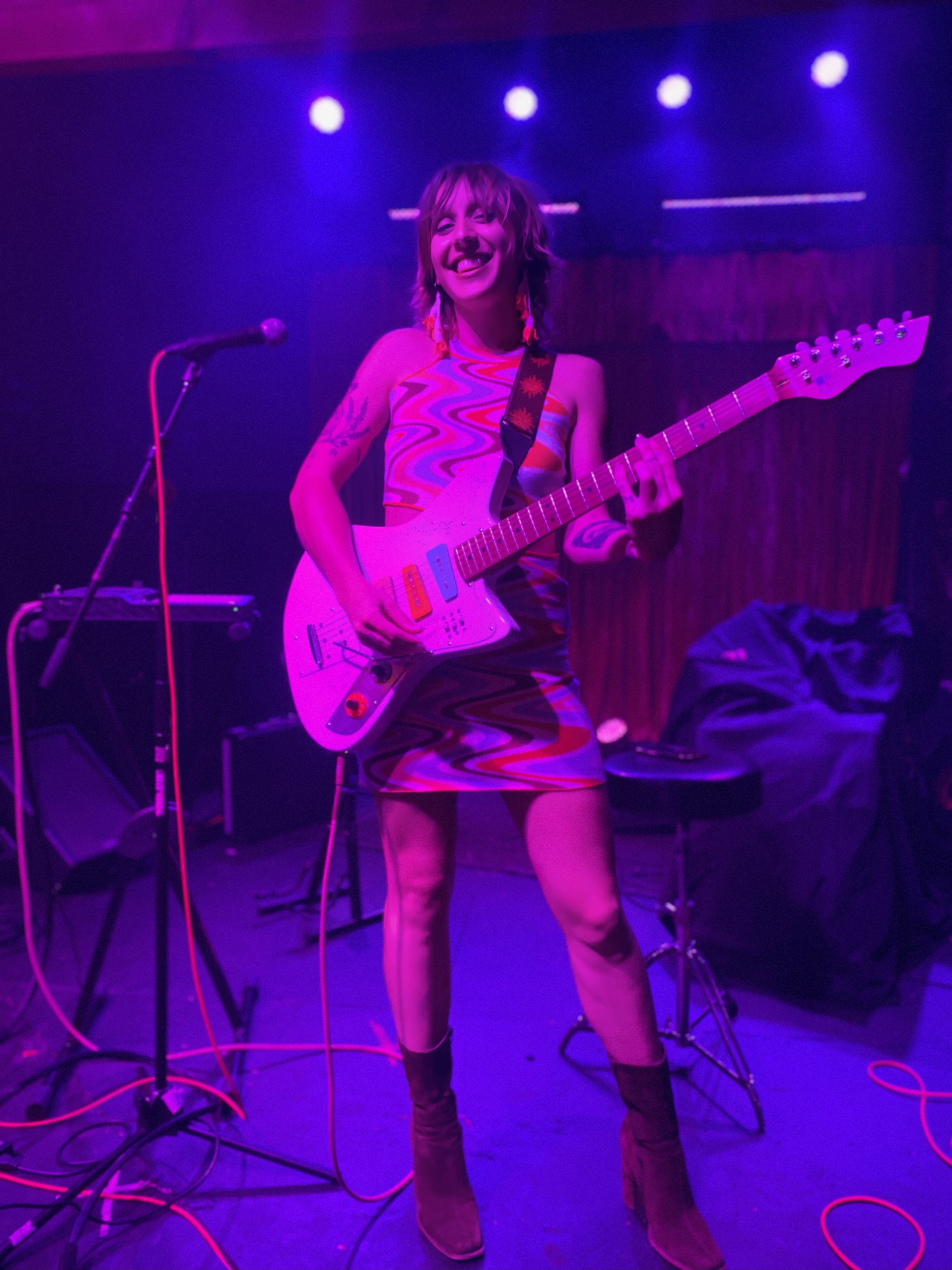 A singer with a guitar smiles as she performed bathed in purple-pink lighting. 