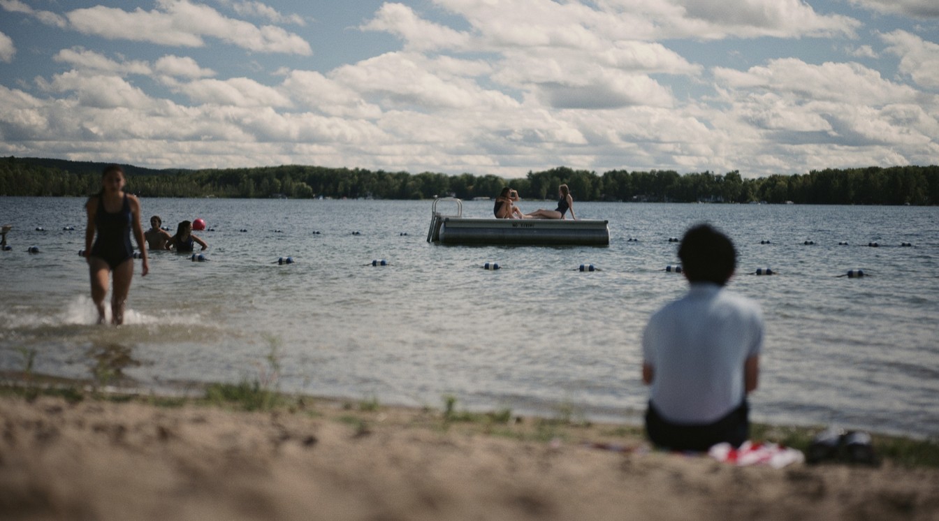 A scene from a film where people are bathing and floating on a lake under a sky with white clouds. 