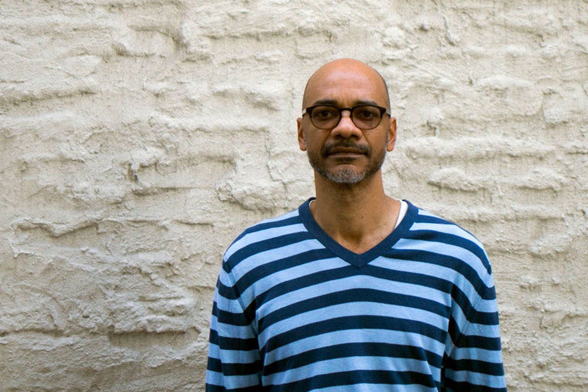 Rodney McMillian in front of a painted brick wall.