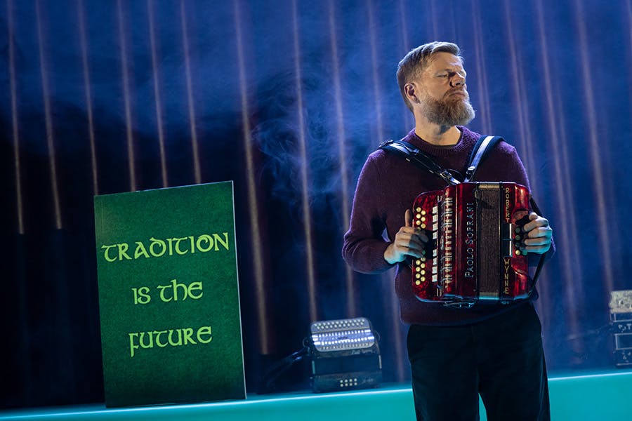 Man performs accordion on stage in front of a sign that reads 'Tradition is the Future'