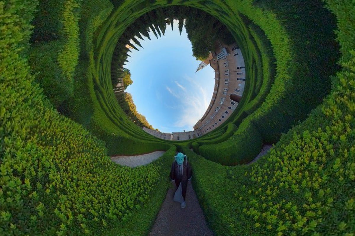 A strange figure walking in an abstract tunnel of greenery with a blue sky at one end