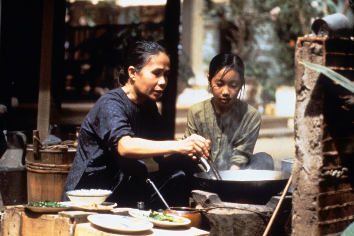 An older woman holding chopsticks in a large pot as a young girl looks on