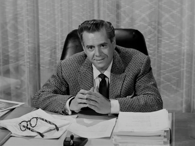 Desi Arnaz in a suit and smiling while seated at a desk