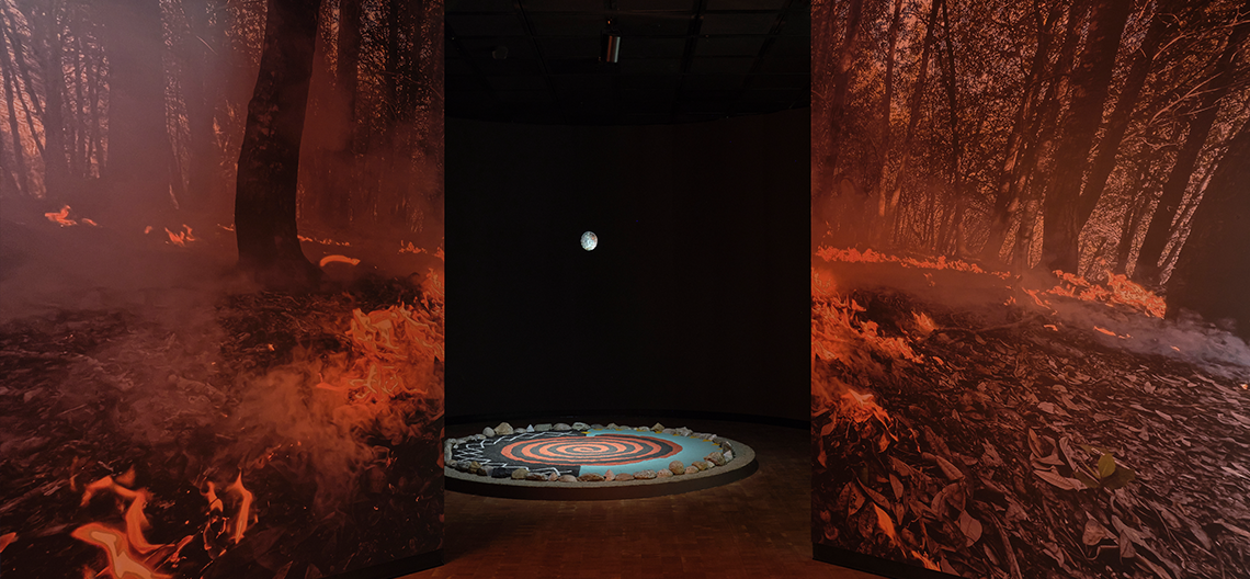 Photo of galleries from Fowler Museum's "Fire Kinship" exhibition. Fire imagery and a sandpainting.