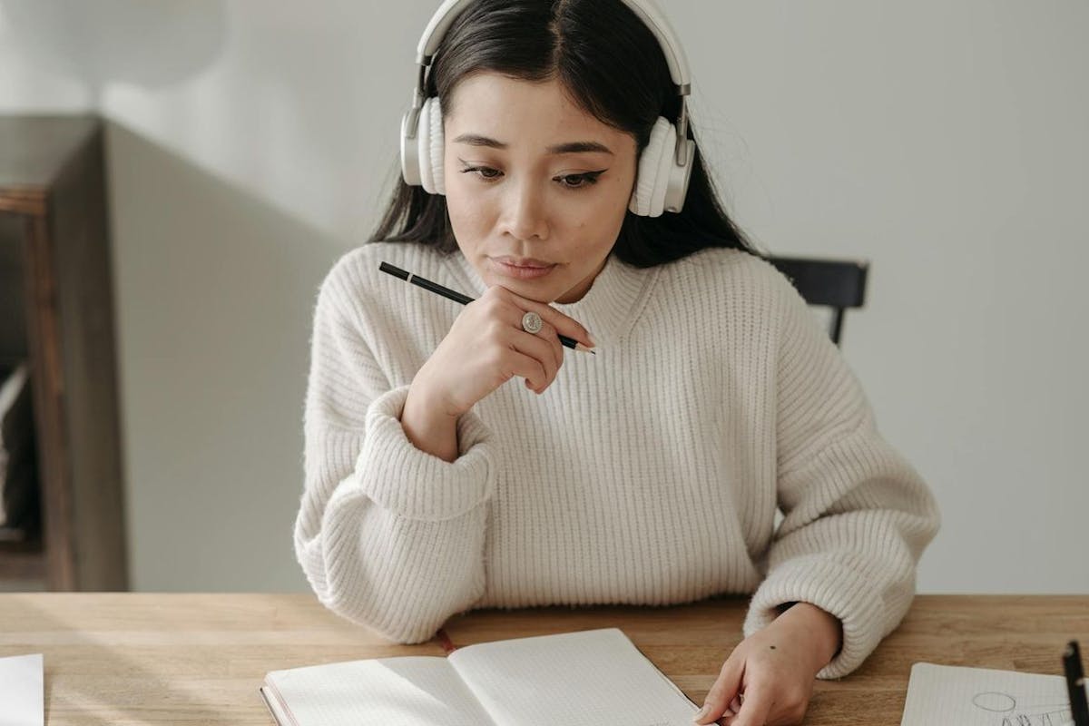 A young woman wearing headphones sits at a desk studying