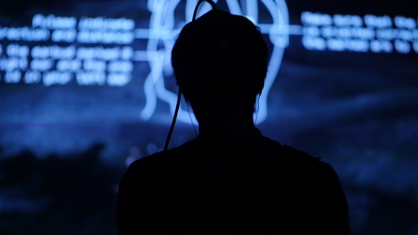 a person with a gaming helmet is seen in the shadow of a blue screen