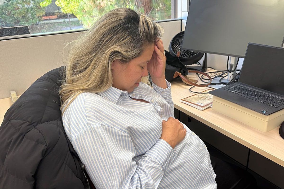 A pregnant woman holds her head as she experiences morning sickness at work.
