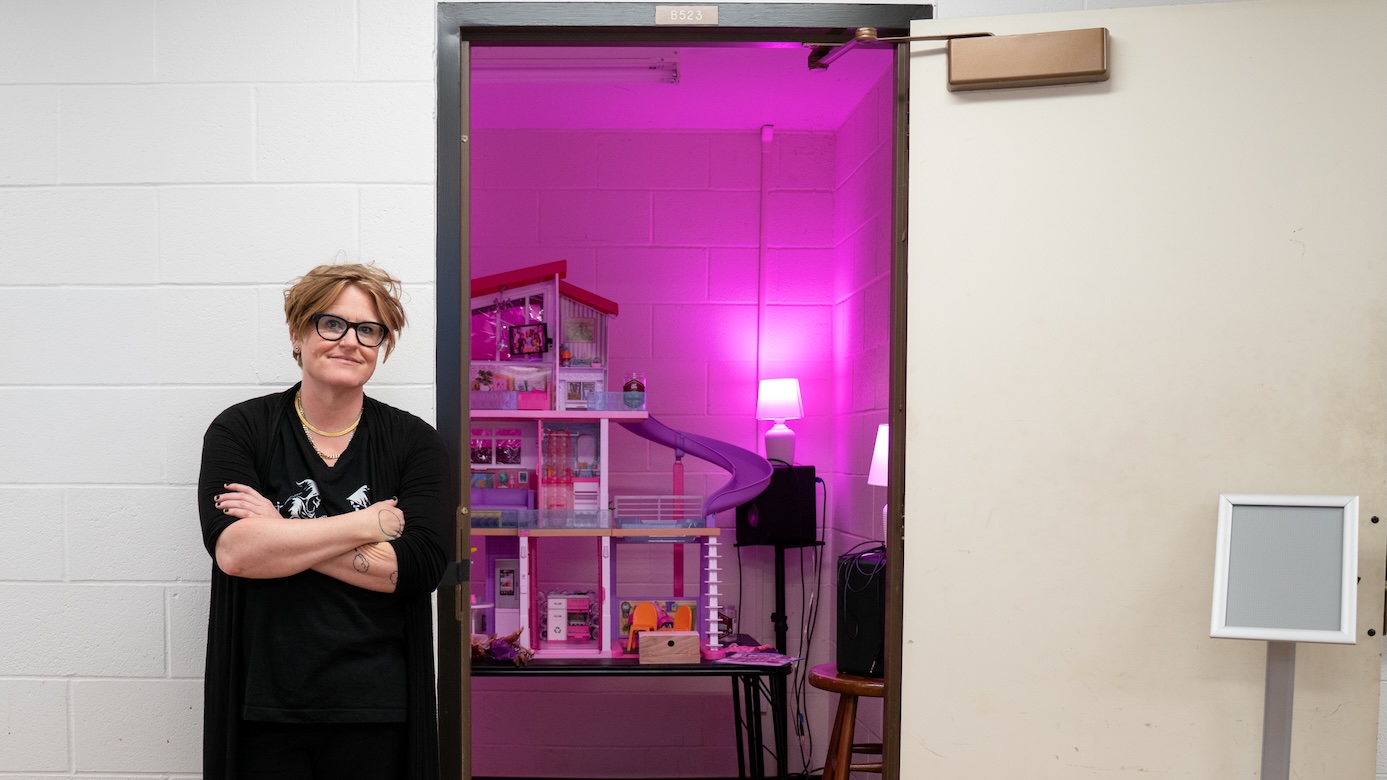Jenny Olivia Johnson poses outside the door of a room that holds her "dreamhouse" exhibition, which is bathed in a pink glow