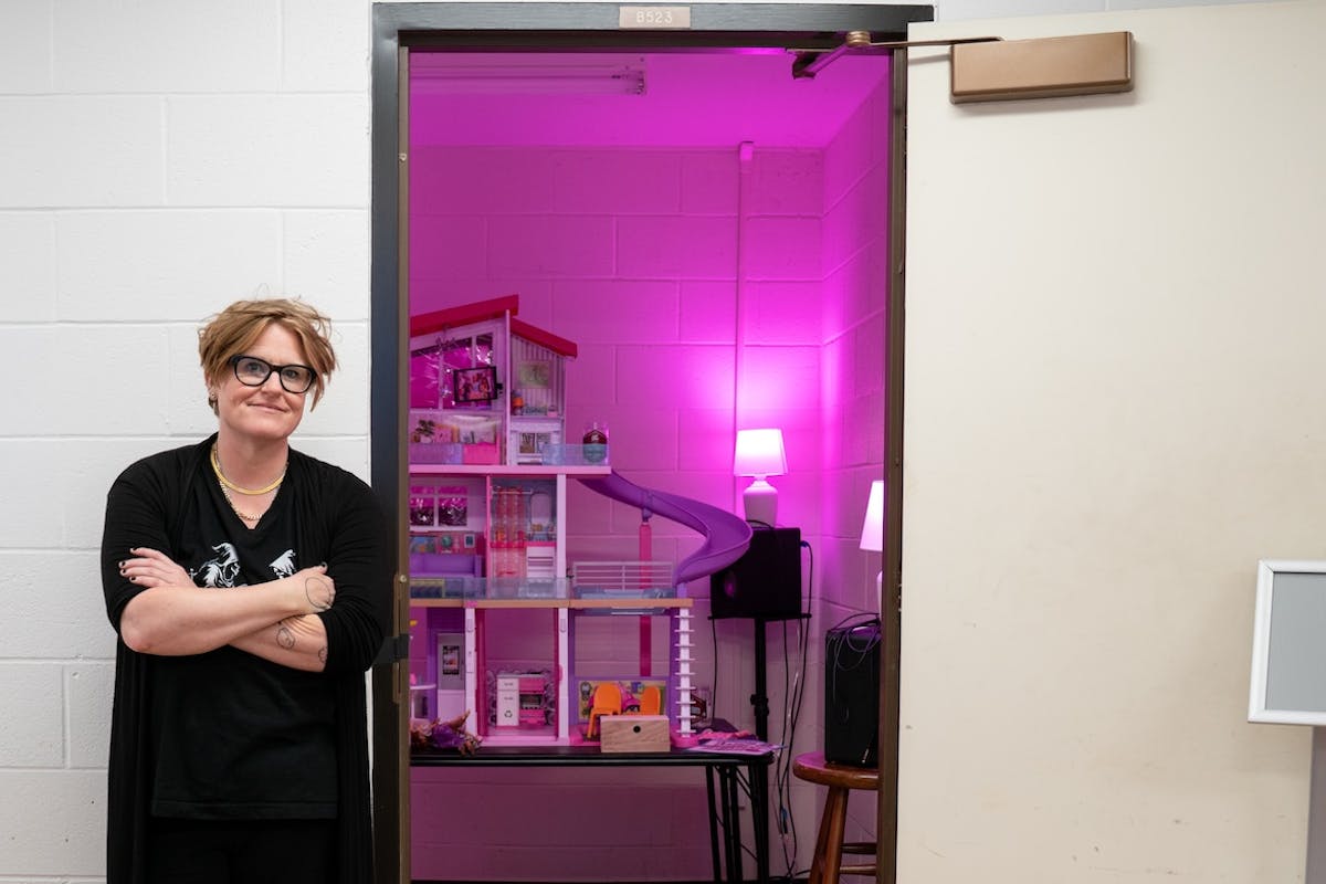 Jenny Olivia Johnson poses outside the door of a room that holds her "dreamhouse" exhibition, which is bathed in a pink glow