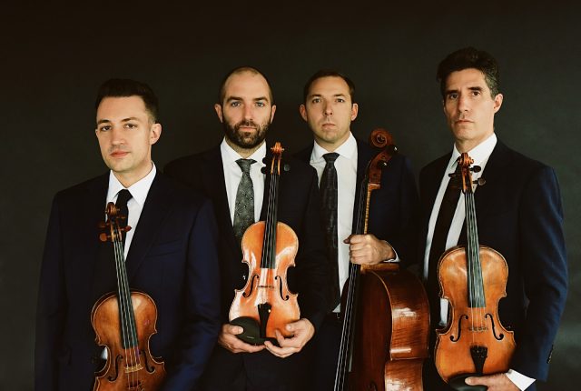 Members of a string quartet pose for the camera with their instruments. Four men wearing black jackets, white suits and ties