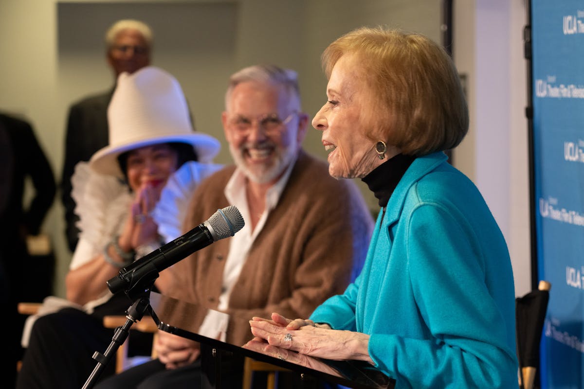 carol burnett speaks at a podium while onlookers smile