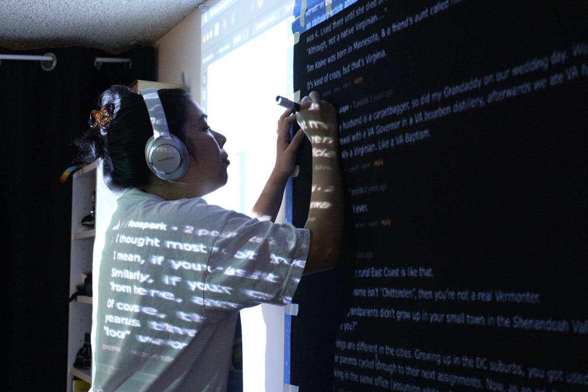 An artist wearing headphones stands in front of a projection of words