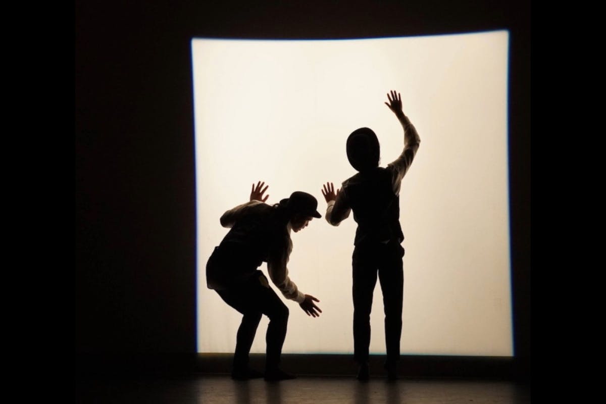 A pair of dancers move in front of a glowing wall