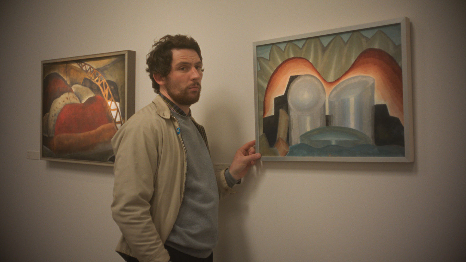 A man stands in a gallery near two pieces of art