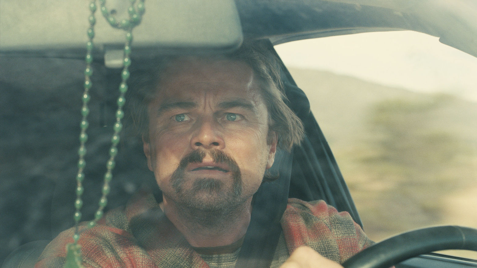 A man played by Leonardo DiCaprio looks out the front window of a car with a disturbed expression