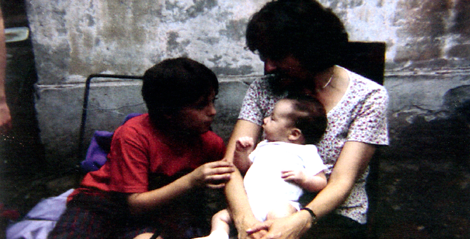 Woman holding a baby with young boy looking on
