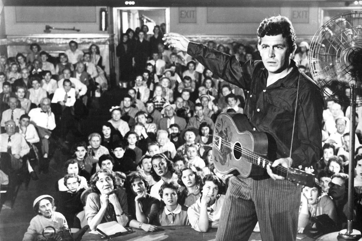 Man with guitar on a stage with audience behind him