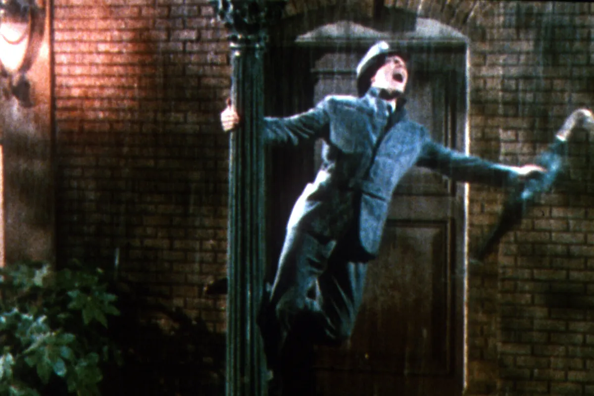 man in suit holding on to streetlamp while singing and holding an umbrella