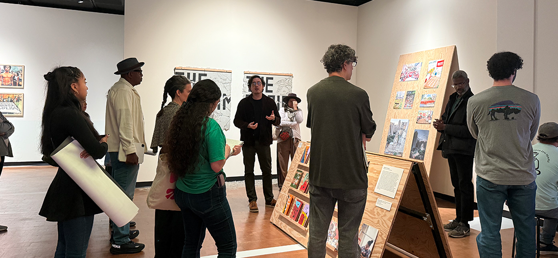 A group of people view art and listen to a talk in a gallery at the Fowler Museum