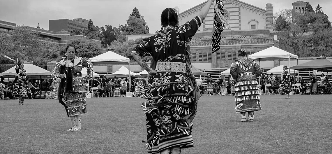 Black and white image of members of native communities in tribal regalia at UCLA Pow Wow