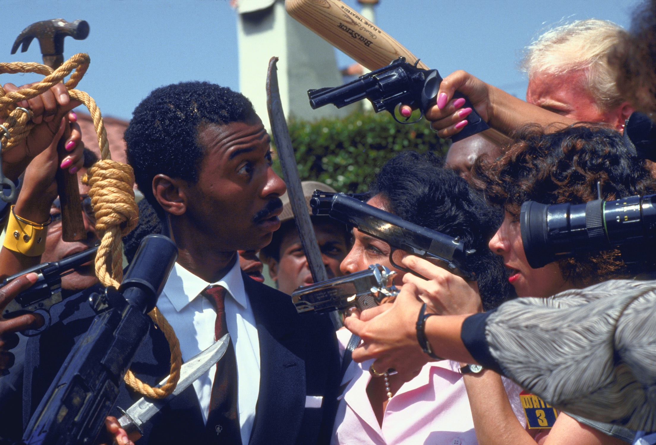 black man in suit with multiple people and guns pointed at his face