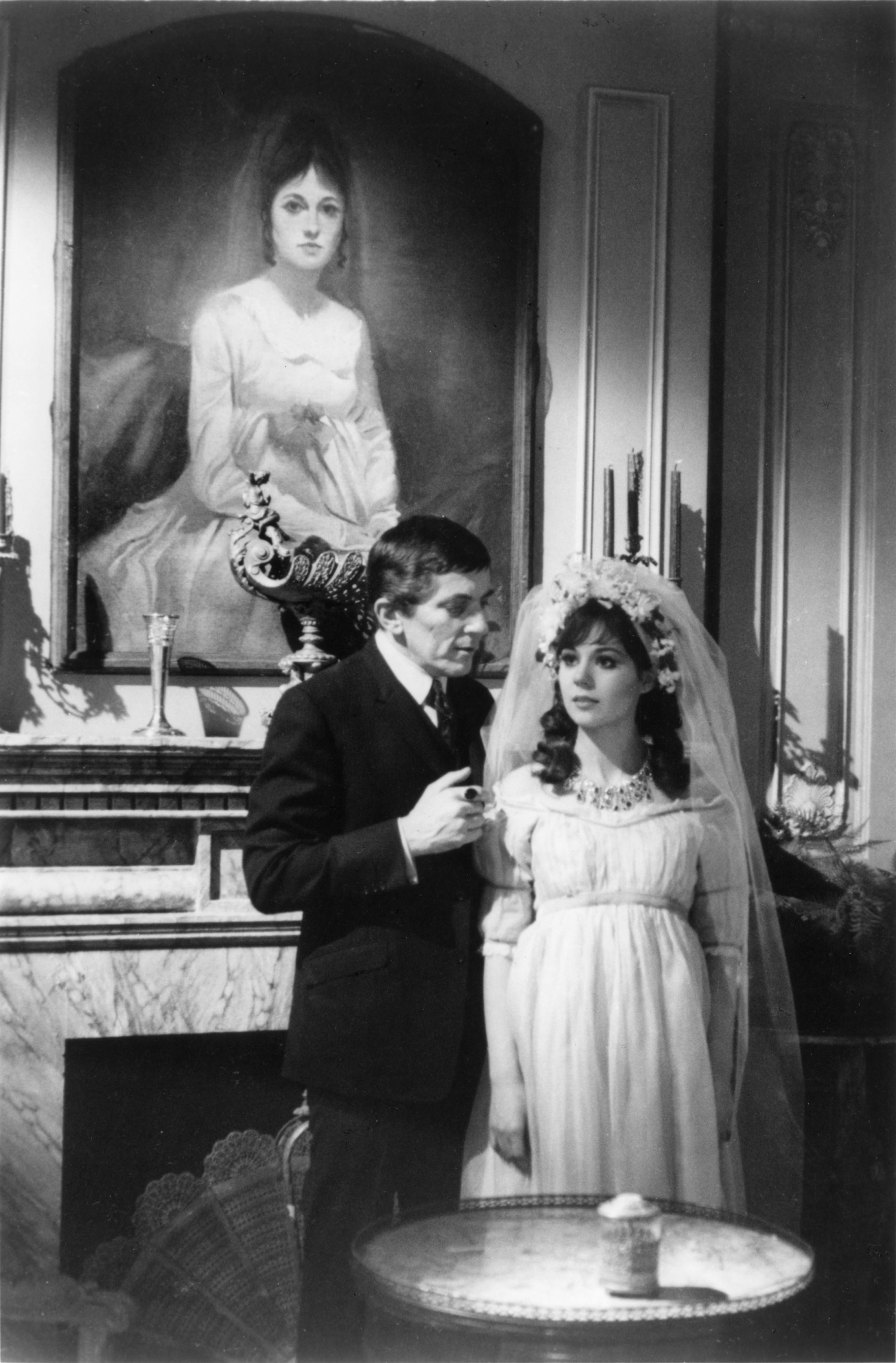 man and woman in gown and veil standing in front of a portrait of woman