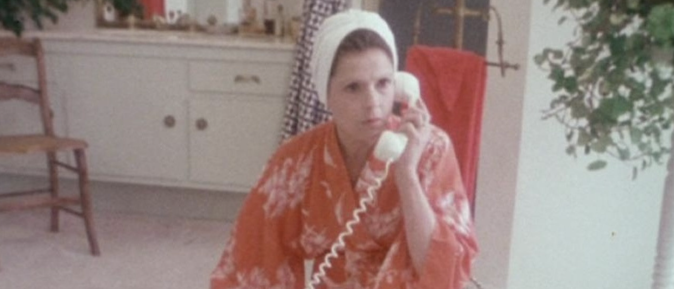 woman wearing robe and hair wrapped in towel holding phone to her ear
