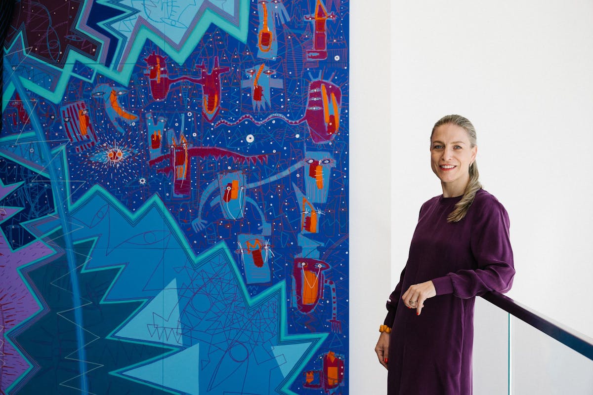 Zoe Ryan, wearing a purple dress, poses near a vibrant artwork wit colors of turquoise and blue. 