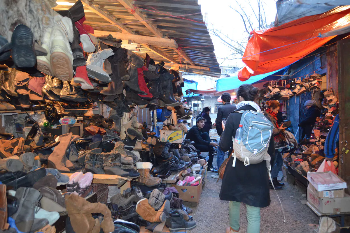 A woman walks down "shoe alley" of a bustling outdoor marketplace.