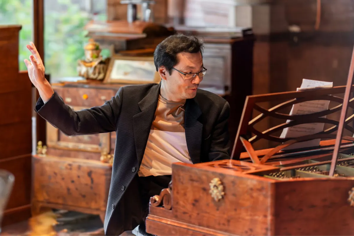 Mike lee sits in a room full of instruments performing on a fortepiano