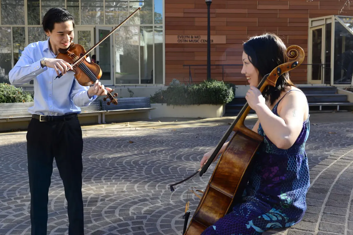A violinist and a cellist facing each other, playing their instrument.