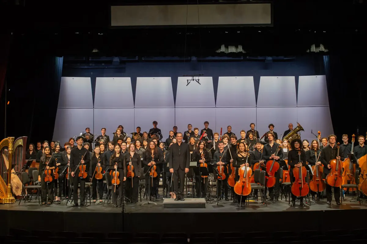 The UCLA Philharmonia on stage, standing up and smiling for the camera.