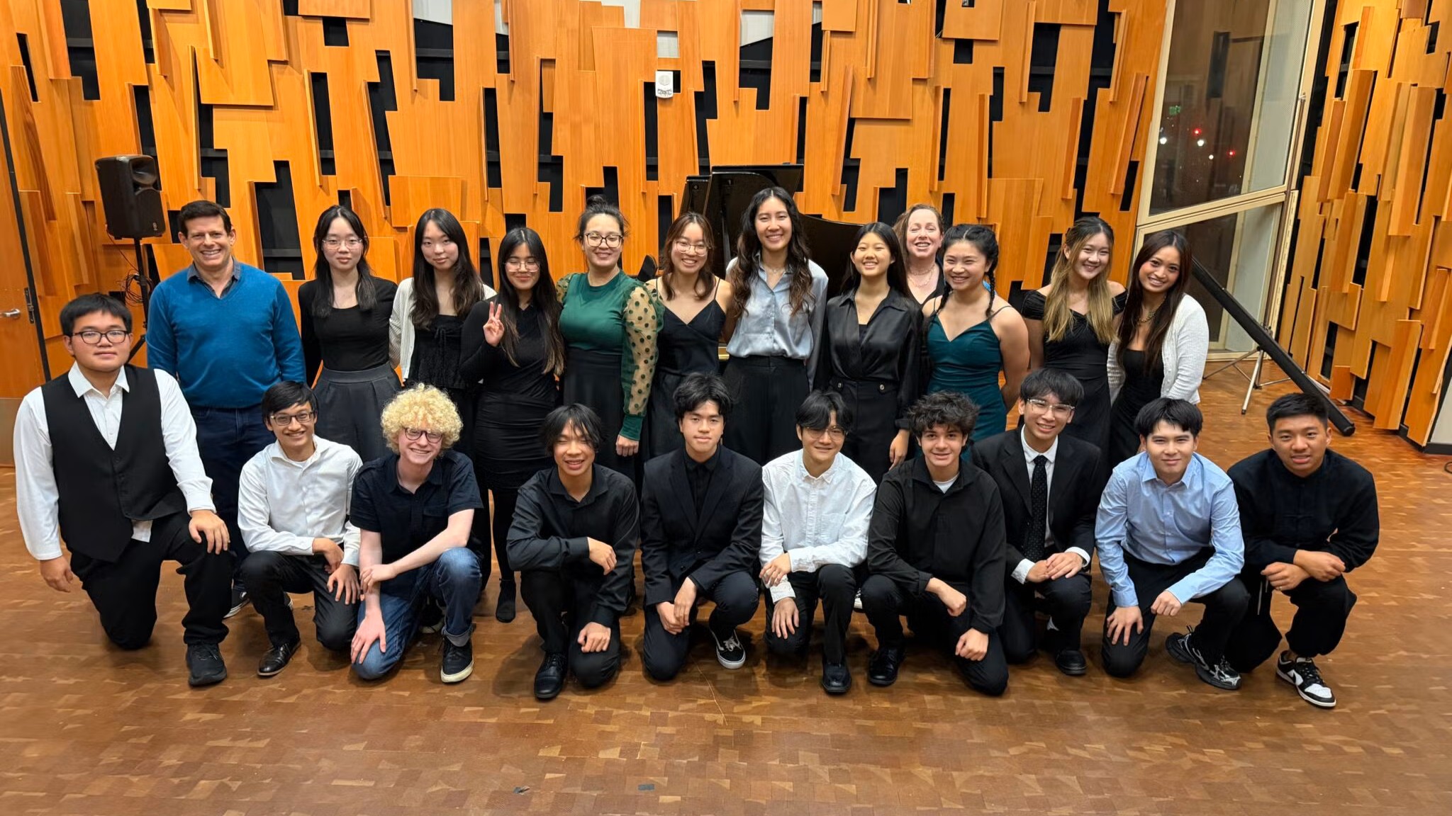 A group of pianists huddle in front of a piano for a class picture.