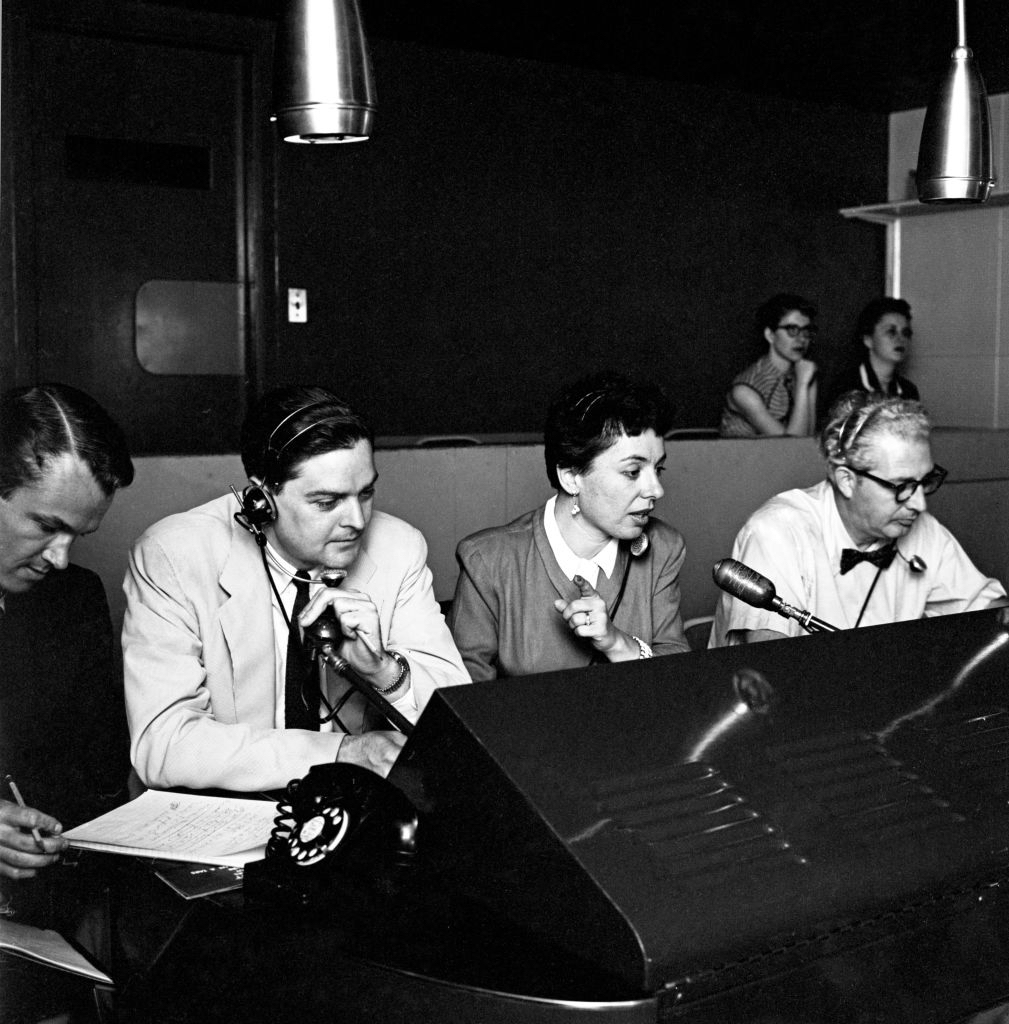 woman seated between two men all seated in front of microphones in a studio