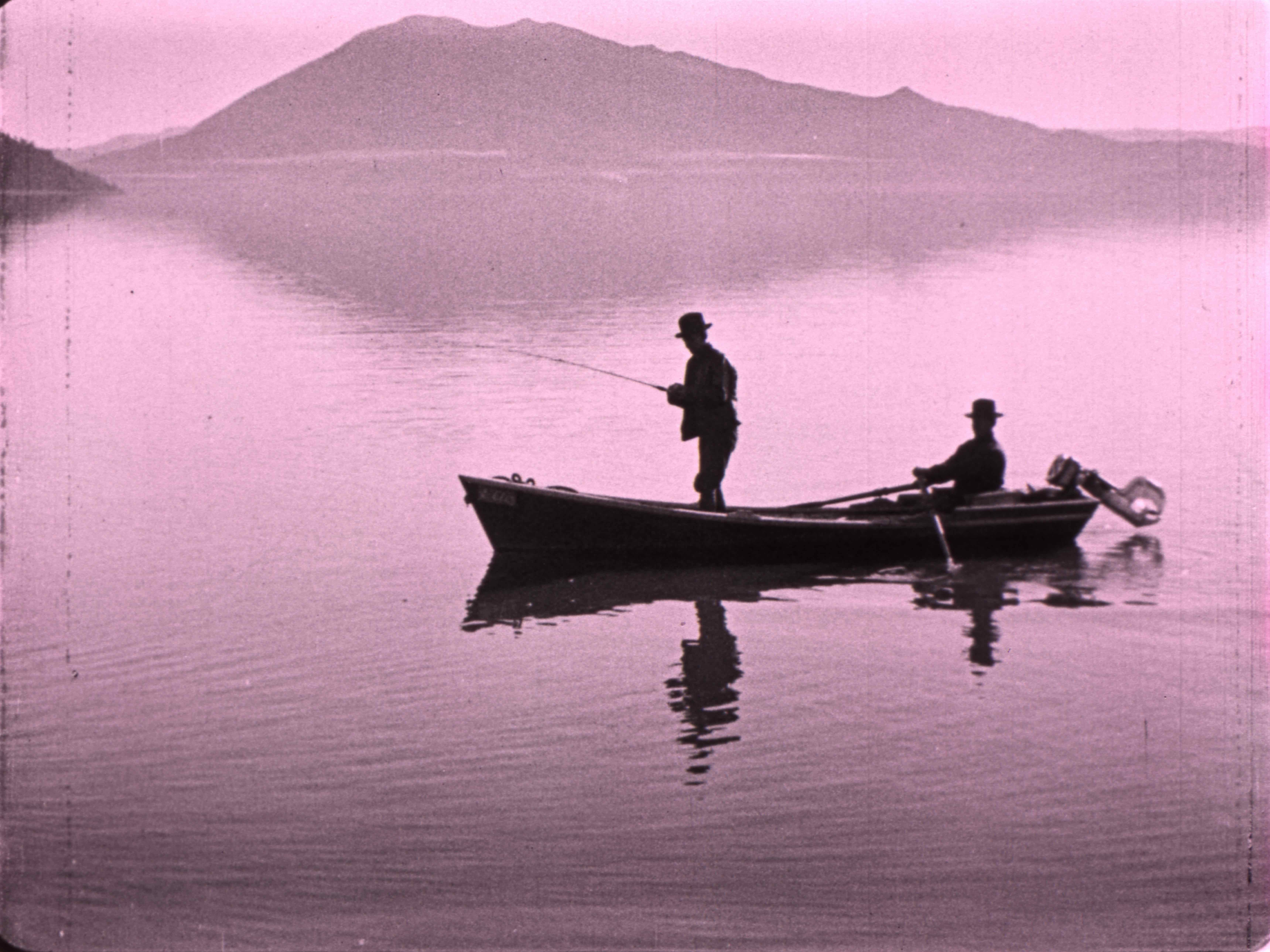 man fishing from boat on body of water with another seated in the boat