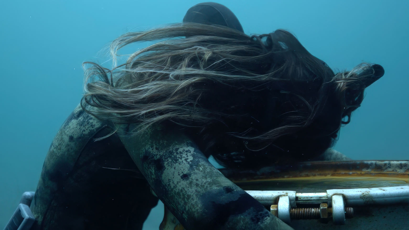 A strange underwater scene, a figure is draped over a corroded barrel.