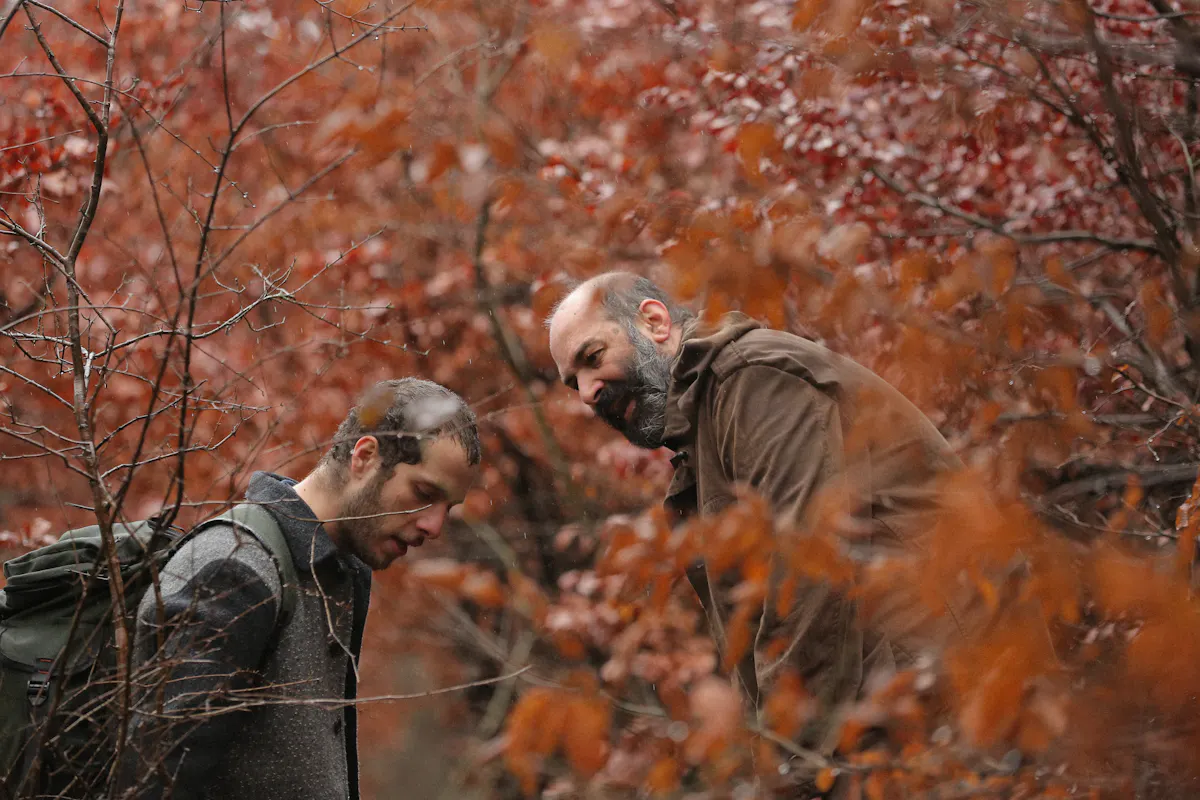 Two men standing surrounded by trees with orange-red leaves