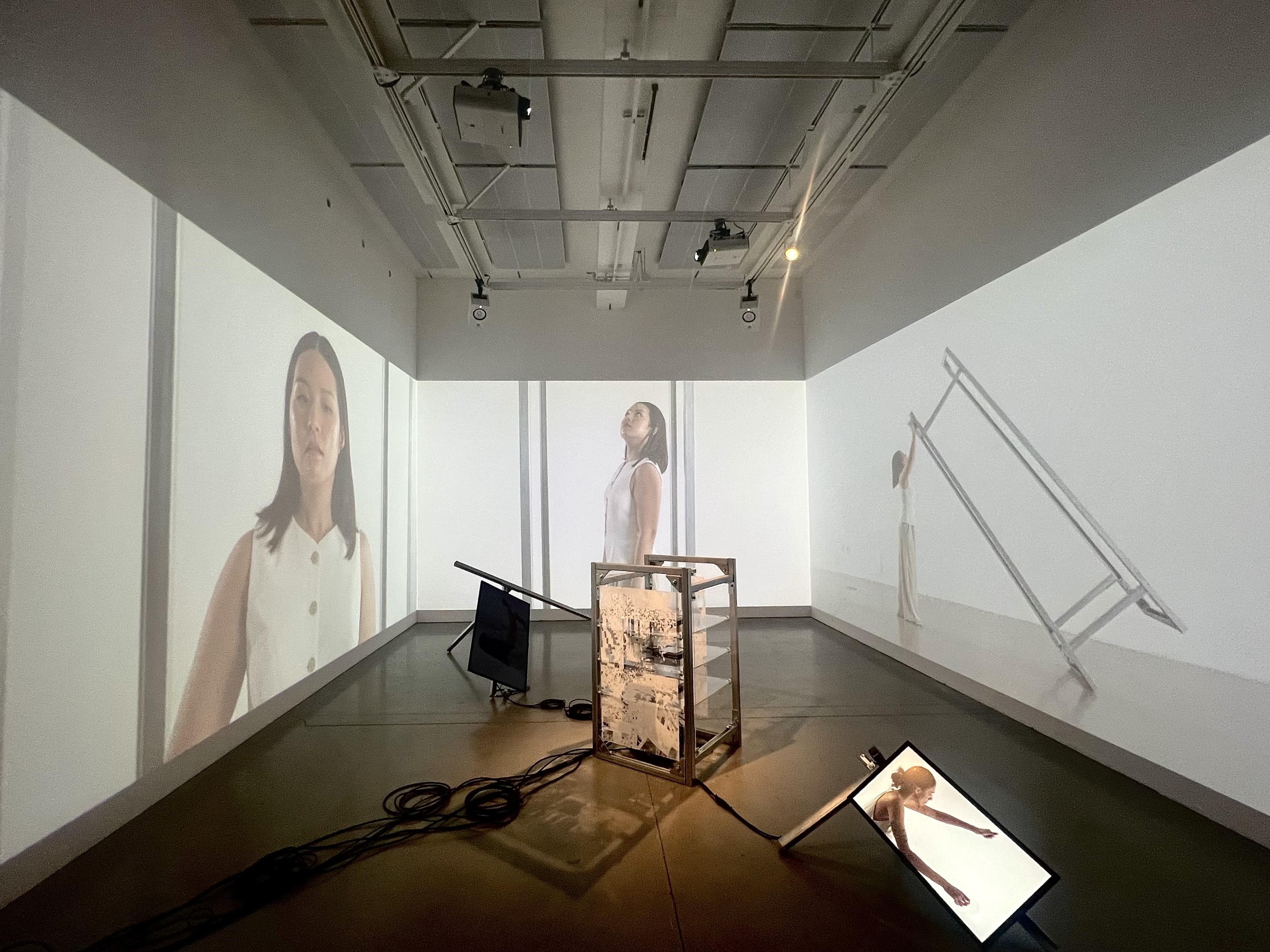 A digital media installation with video on three walls, computer screens on the floor and other metal structures
