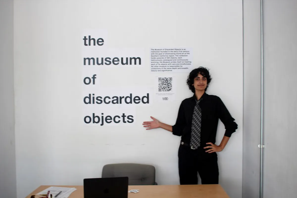 A young person in a tie points to a sign on a white museum wall