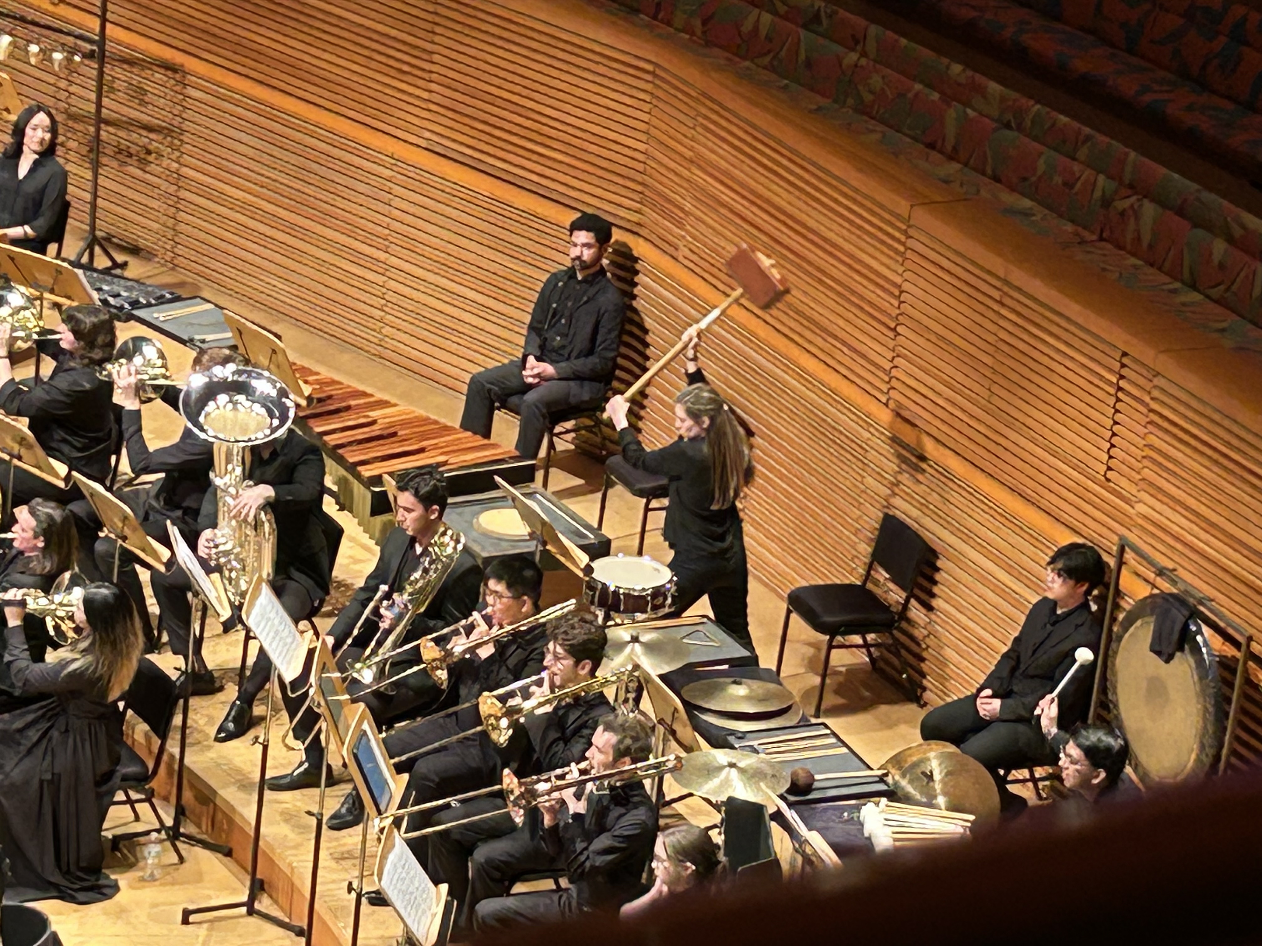 A percussionist prepares to hit a wooden box  with a large wooden hammer