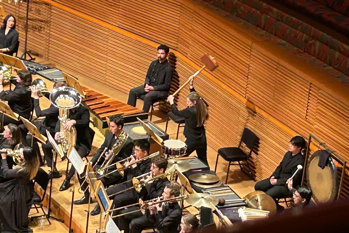 A percussionist prepares to hit a wooden box with a large wooden hammer