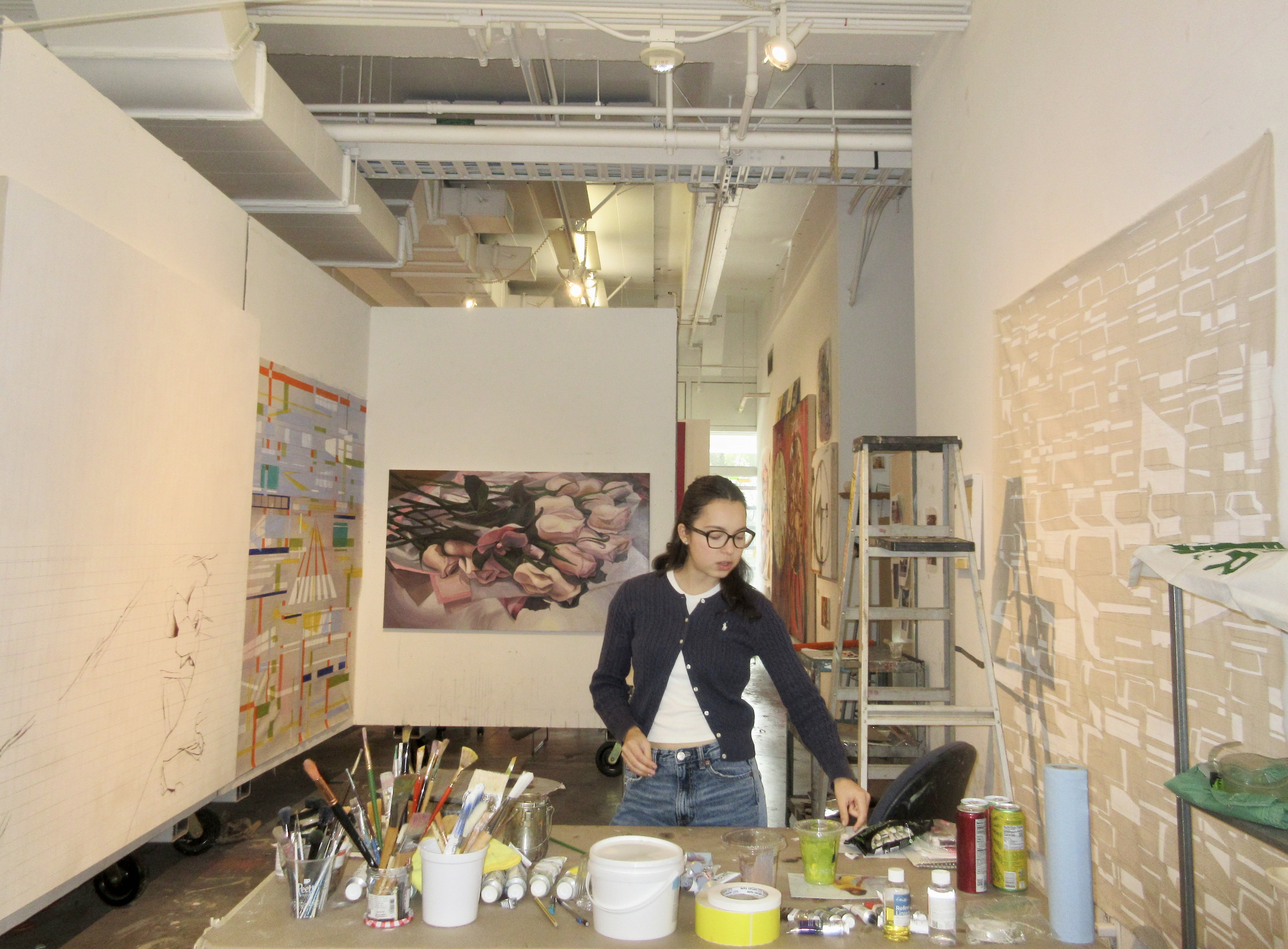 A young woman, surrounded by painting supplies and walls containing her artwork