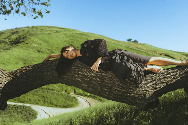 A female dancer poses in dramatic recline on a large tree branch
