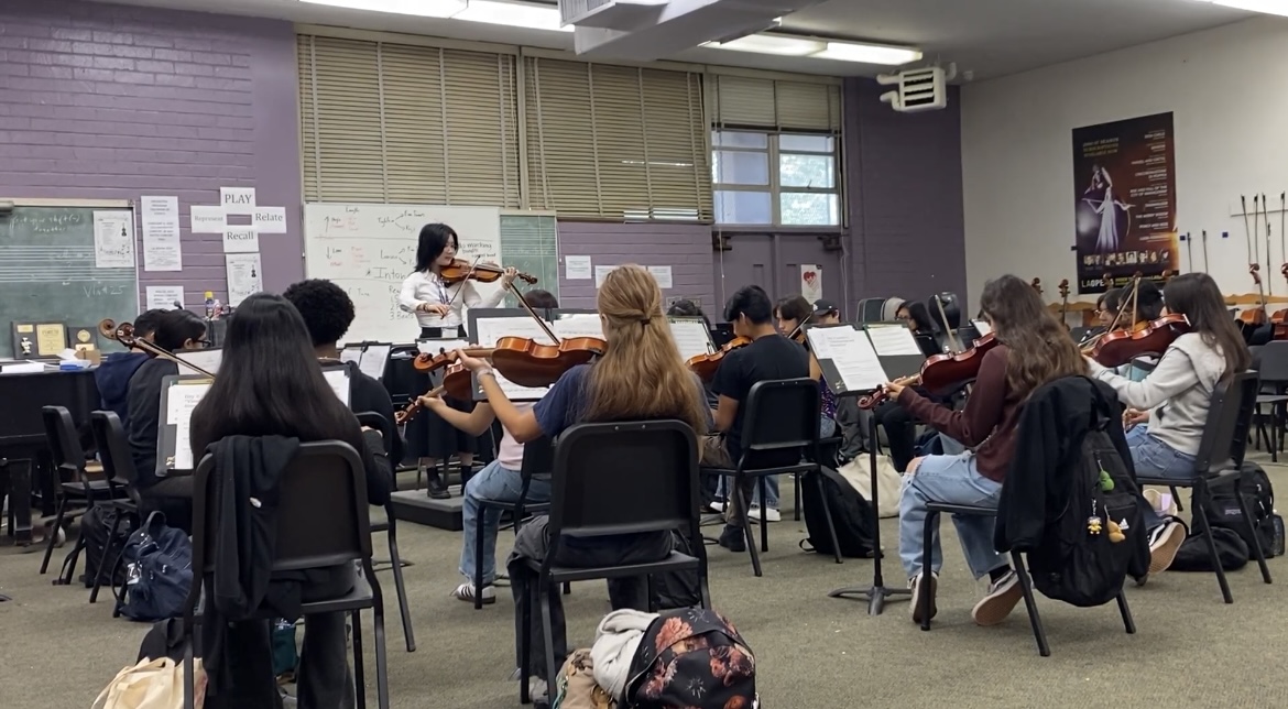 A violin teacher instructs a group of students