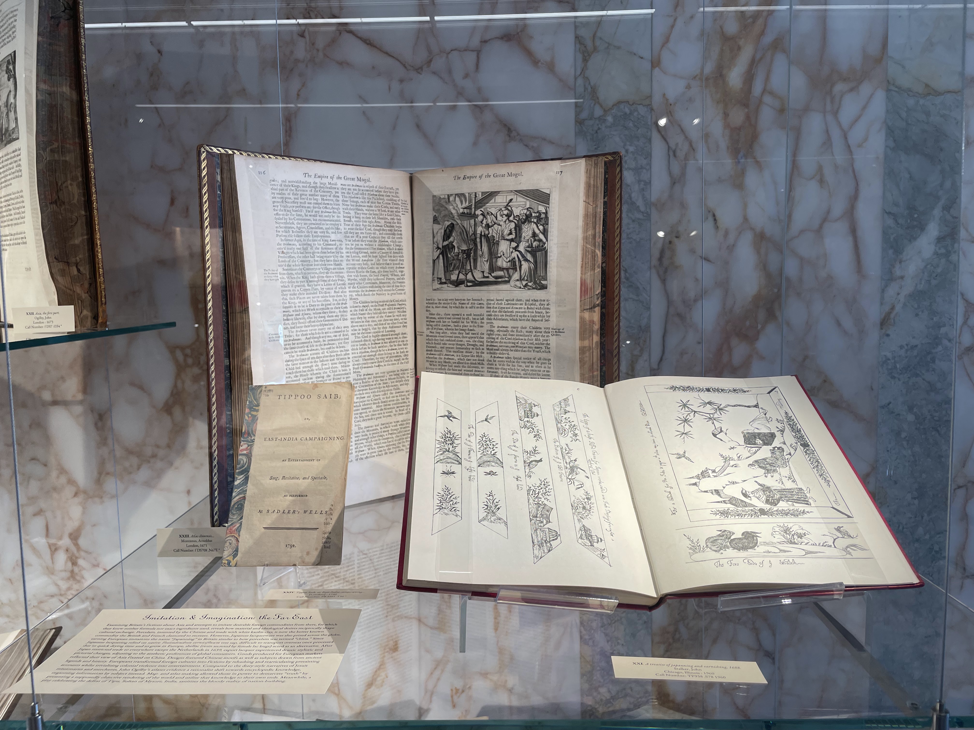Two 18th century books lay open in a glass case
