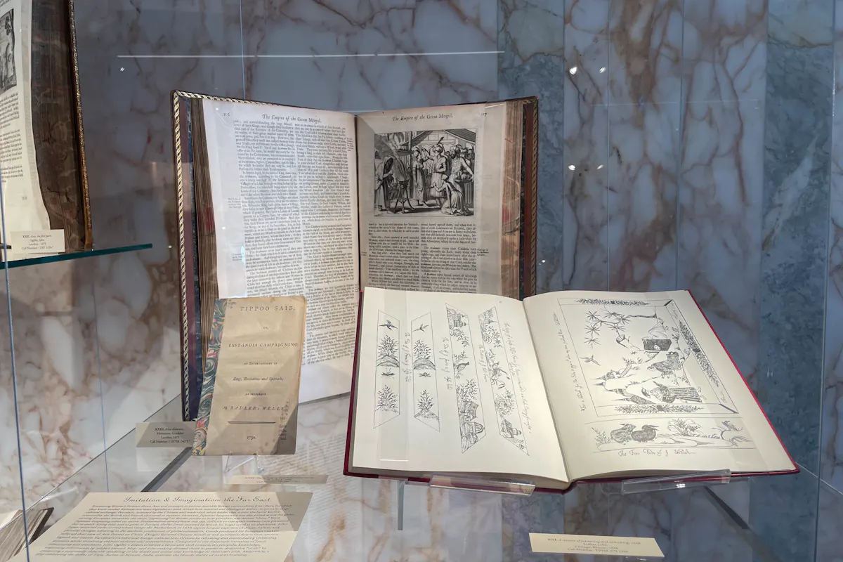 Two 18th century books lay open in a glass case