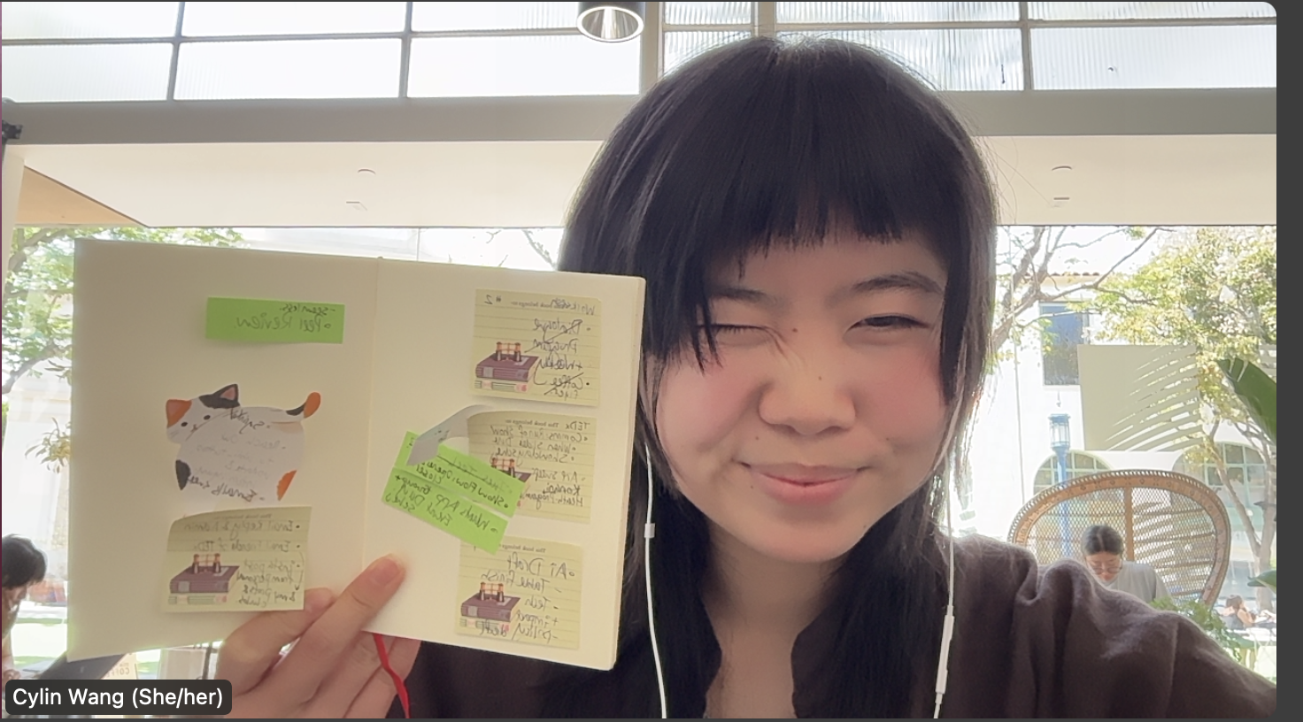 A young woman holds up a page of her journal and winks at the camera